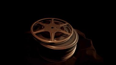 Eski sinema ekipmanlarının dokusunu vurgulayan, karanlık bir arka planda yavaşça dönen klasik metal film makaraları yığını.