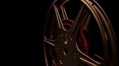 Sinema ekipmanlarının detaylarını gösteren karanlık bir arkaplanda yavaşça dönen tek bir klasik metal film makarasını kapat