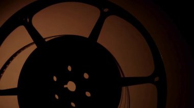 Sinema ekipmanlarının detaylarını gösteren karanlık bir arkaplanda yavaşça dönen tek bir klasik metal film makarasını kapat