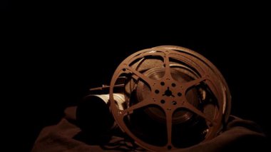 Eski film makaralarının olduğu antika film kamerası karanlık, kapkara bir arka plan stüdyosunun ışıklandırmasına karşı yavaşça dönüyor.