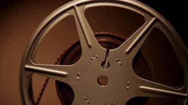 Klasik film makarası, eski sinema ekipmanları ve klasik sinema tarihi estetiğini gösteren sıcak kahverengi bir arka plana doğru yavaşça dönüyor.