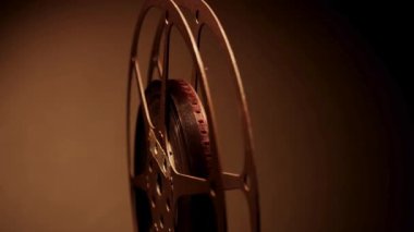 Klasik sinemanın altın çağını anımsatan sıcak bir arka plan karşısında dönen klasik bir film makarasının yakın plan çekimi.