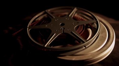 Tarihi film arşivlerinin özünü yansıtan koyu desenli bir kumaş üzerine istiflenmiş birkaç eski film makarası ve metal kaplar.