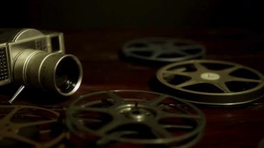 Klasik 8 mm 'lik film kamerası ve birden fazla film makarası karanlık bir odada hafif ışıklandırmanın altında eski bir ahşap masaya saçılmış.