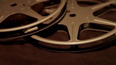 İki klasik metal film, klasik bir sinema görüntüsü için dramatik yan ışıklandırmayla koyu kumaş yüzeyinde yatar.