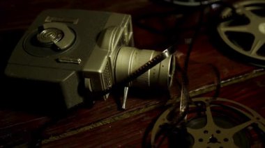 Karmaşık film şeritleri olan eski gümüş renkli sinema kamerası ve sıcak, sade ışık altında karanlık ahşap yüzey üzerinde metal makaralar.