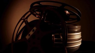 Klasik sinema makaraları ve karanlık bir odada sıcak dramatik ışıklandırma altında karanlık bir yüzeye istiflenmiş metal kaplar.