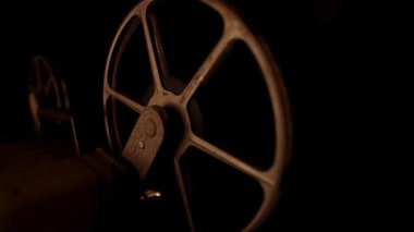 Kaliteli film projektörü, eski sinema yapımı için nostaljik bir atmosfer yaratan sıcak ışıklandırmalı karanlık bir odada dönüyor.