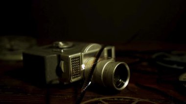 Film makaraları ve dramatik düşük ışıklandırması olan koyu ahşap bir yüzey üzerinde sekiz milimetrelik klasik bir film kamerası yan görüntüsü.