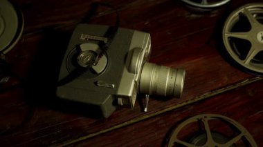 Filmlerle çevrili eski bir film kamerasının yüksek açılı görüntüsü. Karanlık, ahşap bir arka plan ve sıcak, dramatik ışıklandırma.