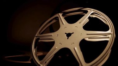 Klasik sinema tarihi ve geleneksel film yapım ekipmanlarını gösteren karanlık bir stüdyoda yavaşça dönen klasik metal film makaraları.