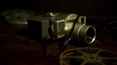 Kırsal ahşap masanın üzerinde duran klasik taşınabilir film kamerası dağınık film makaraları ve iç aydınlatmada selüloit şeritler.