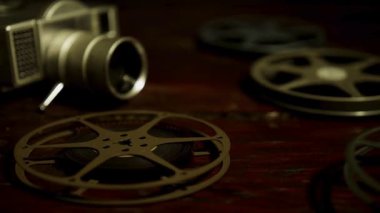 Nostaljik stüdyo ortamında siyah ahşap masanın üzerinde duran klasik film kamerası ve birden fazla metalik film makarasının detaylı görüntüsü