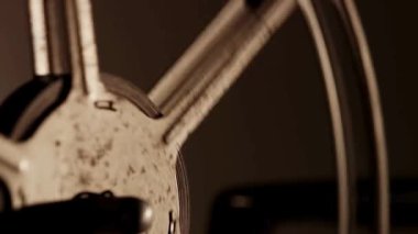 Metalin dokusunu vurgulayan sıcak ışıkla hızla dönen büyük bir klasik metal film makarasının aşırı yakın çekimi.