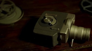 Eski bir film kamerası ve pek çok film, sıcak sinematik ışıklandırmalı, koyu ahşap bir masanın üzerinde dönüyor.