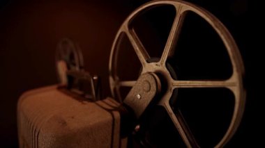 Vintage projektör makinesinde dönen büyük metal film makarasını geleneksel sinema projeksiyon odasındaki karanlık arka plana karşı kapat