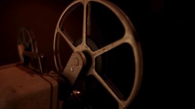 Eski sinema projektörü üzerinde dönen film makarasının düşük açılı görüntüsü klasik sinema filmiyle karanlık odada çalışıyor.