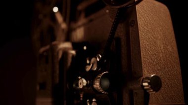 Hareket mekanizması olan klasik film projektörünün yan profili ve sıcak aksanlı aydınlatma ile karanlık stüdyoda film şeridi.