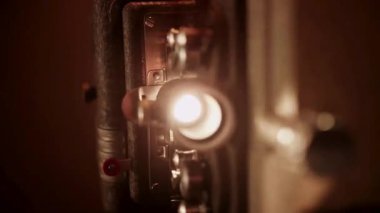 Makro çekim, titreşen ışık demeti ve sığ alan derinliğinde hareket eden mekanik parçalarla vintage projektör merceğine odaklanıyor.