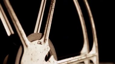 Eski endüstriyel dokuları ve klasik sinema tarihini vurgulayarak karanlık odada hızla dönen paslı metalik film makarasının aşırı yakın çekimi