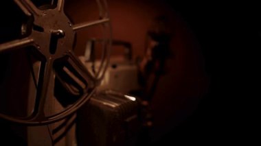 Karanlık odada dönen makaraları ve sinematik atmosferi aydınlatan sıcak spot ışıklarıyla çalışan klasik film projektörünün geniş açılı görüntüsü