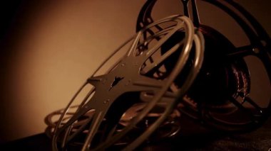 Sıcak, kasvetli ışıklandırma ortamında karanlık masanın üzerinde gevşek film şeritleriyle birbirine yaslanmış birden fazla klasik film makarası.