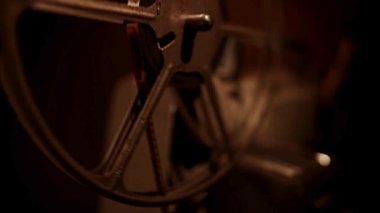 Klasik film makarası, film gösteriminde eski projektörün üzerinde dönüyor. Karanlık odada, sıcak, parlak ışıklandırmalı klasik film gösterimi sırasında.