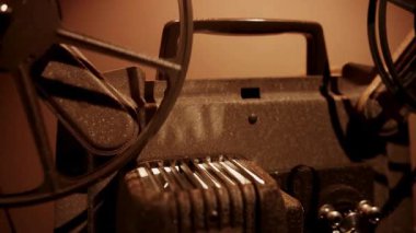 Klasik film projektör mekanizması, film şeritleri hareket ediyor ve karanlık bir odada retro sinema gösterisi sırasında makaralar dönüyor.