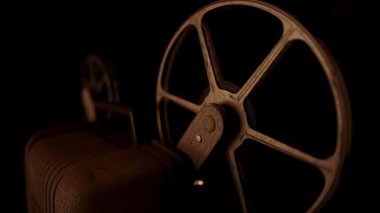 Klasik klasik bir film projektörünün arka ışıklandırılmış silueti. Sıcak ortam aydınlatmalı, karanlık bir stüdyoda iki dönen makarası var.