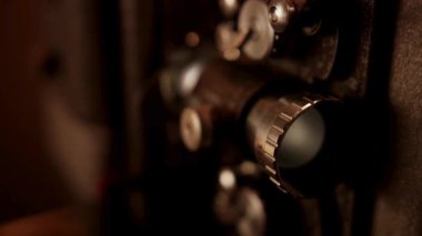 Lensin ayrıntılı görüntüsü ve açıklık kontrolleri, karanlıkta yumuşak, sıcak kapalı bir ışığın altında, klasik bir sinema kamerasında.