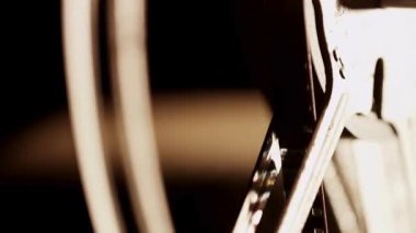Yüksek kontrastlı karanlık bir ortamda tellerin içinden selüloit film geçen eski bir film projektörünün dönen makarası.