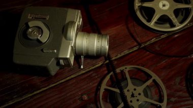 Klasik sinematik film projektörü ve metal makaraları eski ve nostaljik bir oda ortamında sıcak ışıklandırmayla birlikte koyu ahşap masanın üzerinde uzanıyorlar.