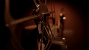 Karanlık bir sinema salonundaki geleneksel film gösterimi sırasında klasik bir projektörde dönen metal bir filmin detaylı görüntüsü.