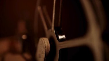 Eski bir sinemanın dönen makaraları karanlık bir odada yavaşça dönüyor ve metalin üzerinde çarpıcı bir şekilde sıcak renklendiriliyor.