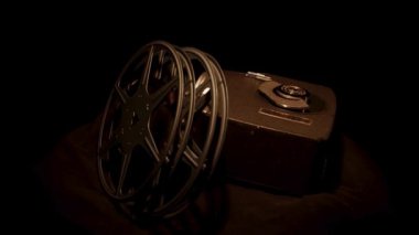 Eski bir film projektörünün dönüşümlü görüntüsü ve sıcak dramatik ışıklandırmalı siyah kumaş yüzeyi üzerinde birkaç metal makara.