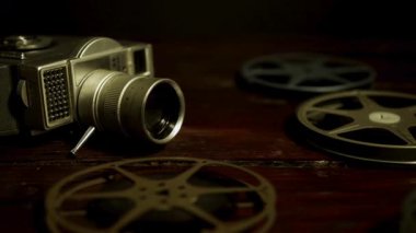 Antika 8 mm film kamerası ve metal makaralar klasik sinematik hikaye anlatımı ve tarihi film projeleri için ahşap bir masanın üzerinde yatıyor.
