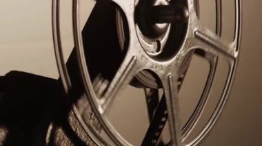 Yüksek açılı bir metal film makarası klasik bir projektörün üzerinde dönüyor ve mekanizma boyunca film şeridi hareket ediyor.