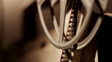 Kaliteli bir sinema projektörünün metal makaralarından geçen ince bir film şeridine aşırı yakın çekim.