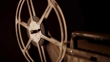 Eski bir projektör film makarasının yakın çekim görüntüsü. Koyu desenli metal arka planda sürücü kayışı görünür.