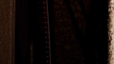 Dikey film şeridi, eski bir film projektör mekanizmasının kapısından çekilerek son derece yüksek kontrastta gösteriliyor.