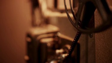 Dönen makaraları ve mekanik gövdeyi yumuşak odaklı ılık ışıklandırmada gösteren klasik bir film projektörünün yan perspektifi