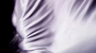 Zarif mor ipek kumaş yavaş çekimde koyu bir arkaplana doğru akarak pürüzsüz dalgalar ve arka plan için lüks bir doku yaratır.