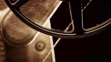 Bir projektörün içinde dönen klasik film makarasını kapatın. Sıcak sepia tonlarıyla ve dönen film filmine odaklanan sinematik ışıkla.
