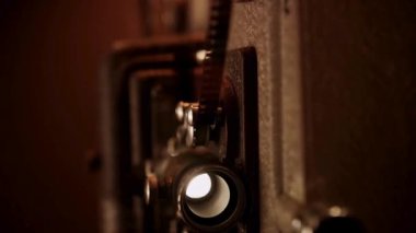Eskimiş film projektörü karanlık bir odada, parlak bir ışıkla objektifin içinden geçiyor ve eski film makarası dönüyor.