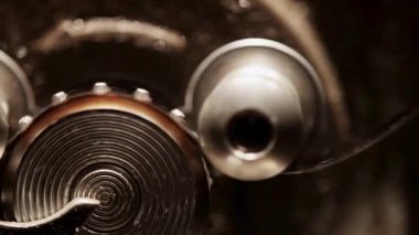 Çelikten yansıyan sıcak ışıkla eski bir mekanik cihazın içinde dönen metal dişlilerin ve dairesel dişlilerin makro görüntüsü