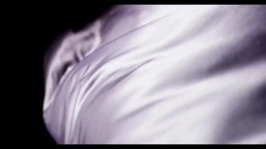 Zarif beyaz ipek kumaş, siyah bir zemine doğru zarif bir şekilde akıyor. Stüdyo ortamında yumuşak dalgalar ve yumuşak dalgalar yaratıyor.