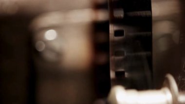 Sinematik ışıklandırma ve bokeh ile karanlık odada bir film projektör mekanizması aracılığıyla çalışan klasik 35 mm film şeridini kapat