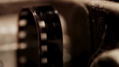 35 mm 'lik film şeridi, klasik bir film projektörünün çarkının üzerinde hareket ediyor. Karanlık sinema ortamında.