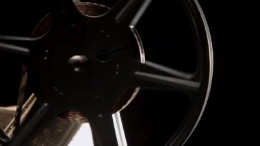 Bir film projektörünün üzerinde dönen selüloit bantla dönen klasik film makarası yakın çekim sinemasında koyu bir arkaplana karşı.