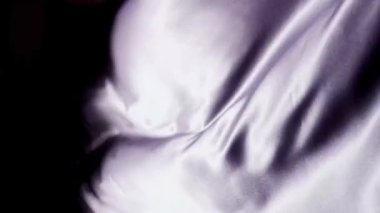 Zarif beyaz ipek kumaş yumuşak dalgalanmalar ve yumuşak röfleler ile yavaş çekimde koyu bir arka plana doğru sallanıyor.